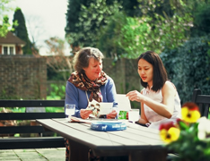 A young homestay student learning English with woman at a table outside in a garden